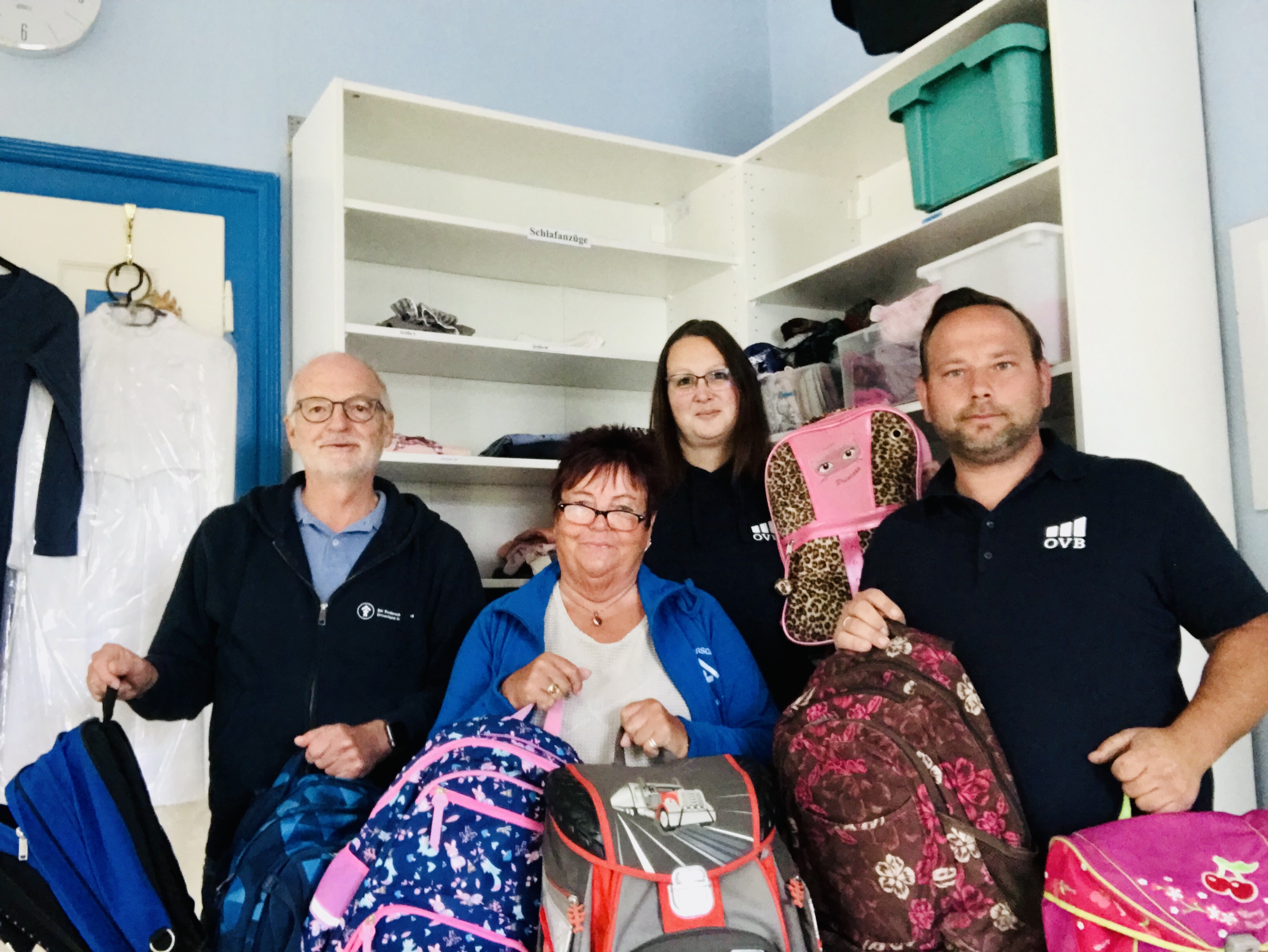 Zwei Männer und Zwei Frauen mit Schulranzen stehen vor Regal