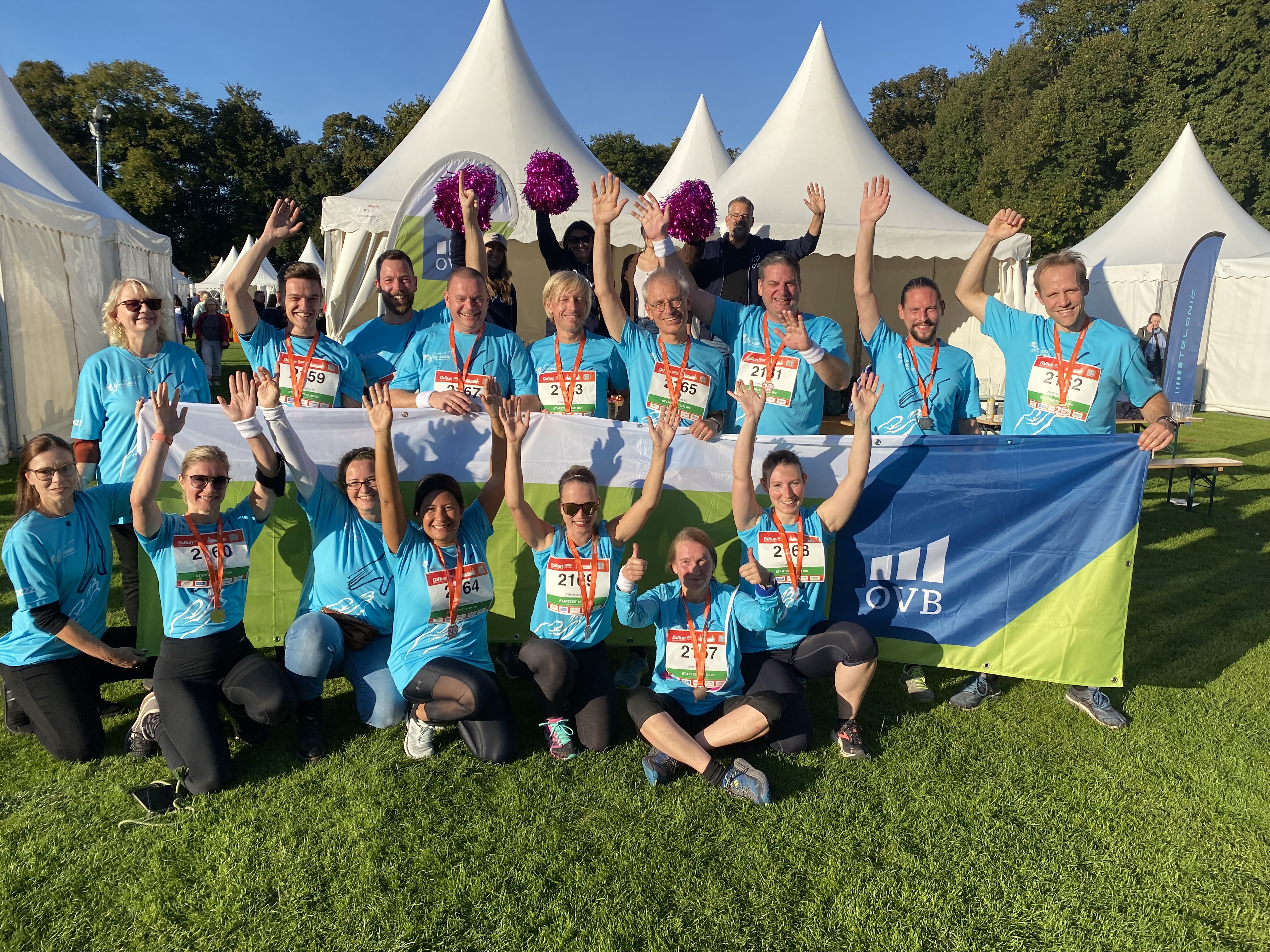 OVB Mitarbeiter beim B2Run in Köln halten einen Banner hoch und winken. Es ist Sommer und sehr warm